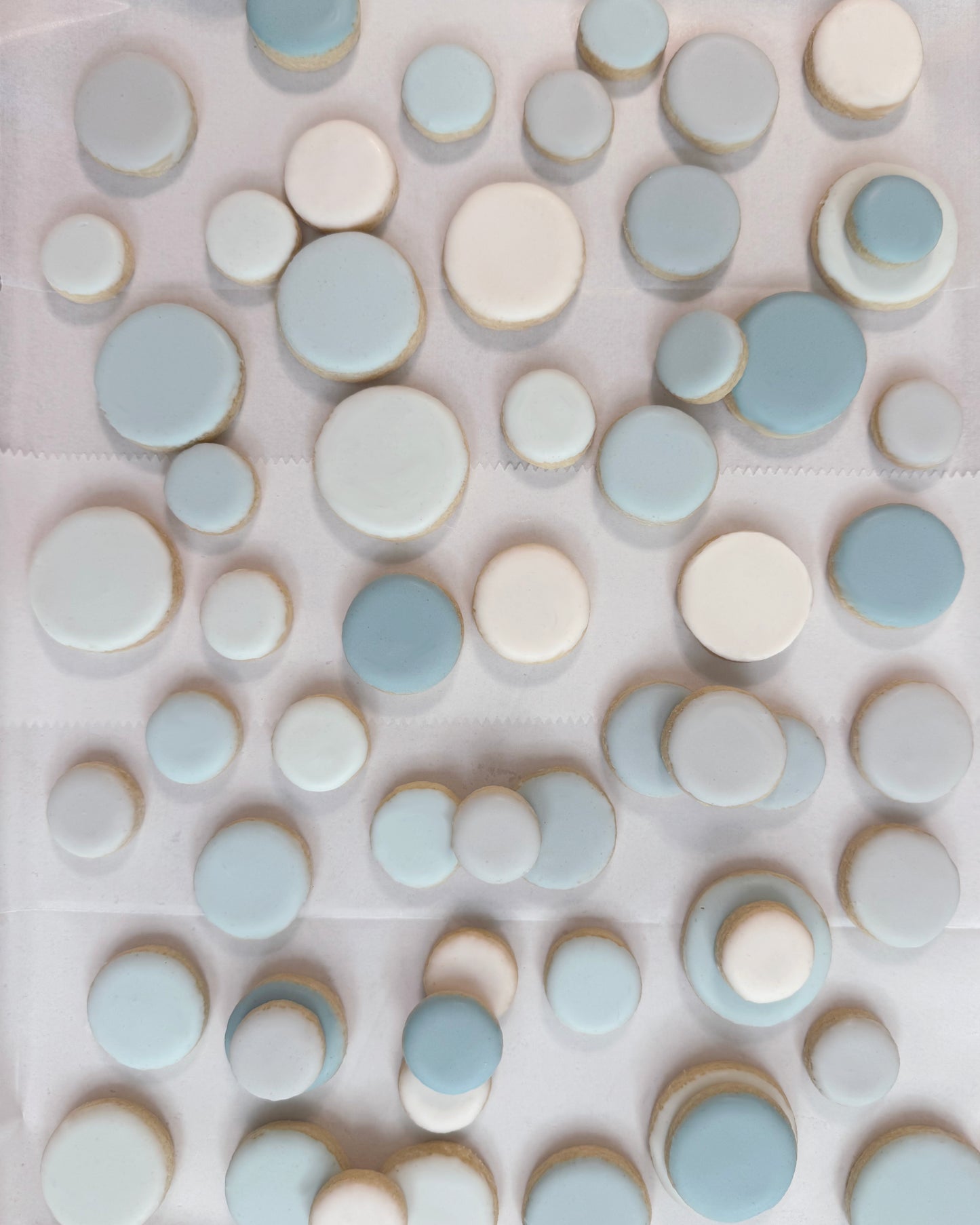 Assorted iced sugar cookies in soft blue and ivory tones in varied small round sizes