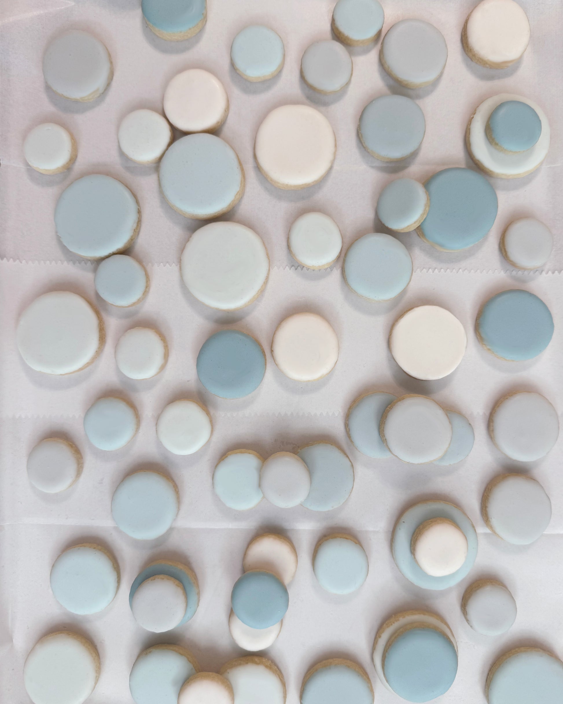 Assorted iced sugar cookies in soft blue and ivory tones in varied small round sizes